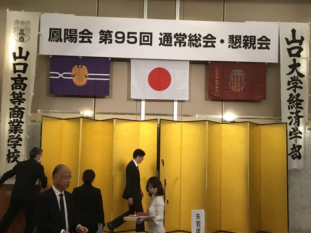 アルカディア市ヶ谷富士の間 舞台上には総会看板その下には真ん中に日の丸左右に高商・経済学部ノの旗左右高商・経済学部の幟